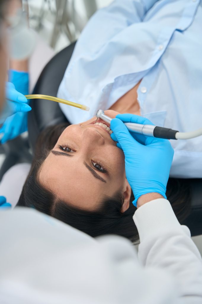 Top-view dental technician using dental drill, treating teeth of client
