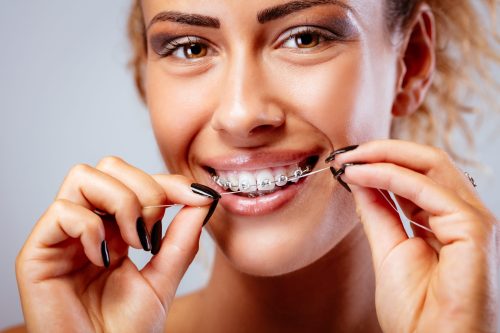 Close-up of a smiling girl with braces cleaning teeth with dental floss. Looking at camera.